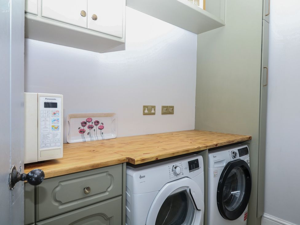 A laundry room with a washing machine, tumble dryer, and countertop at The White House in Okehampton