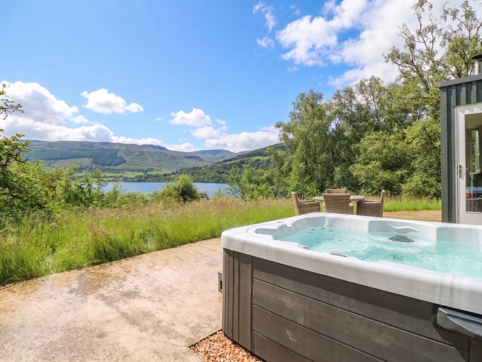 An outdoor area with a hot tub and seating overlooking a lake at The Tractor Shed in Killin