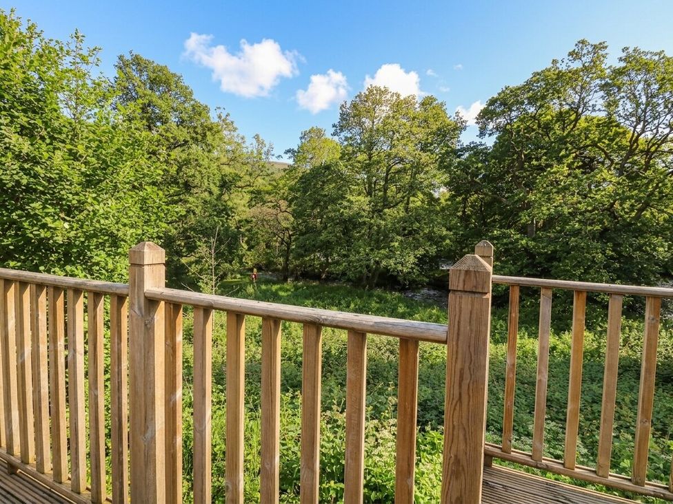A view from a wooden deck overlooking trees and a river at Garth Cottage in Killin
