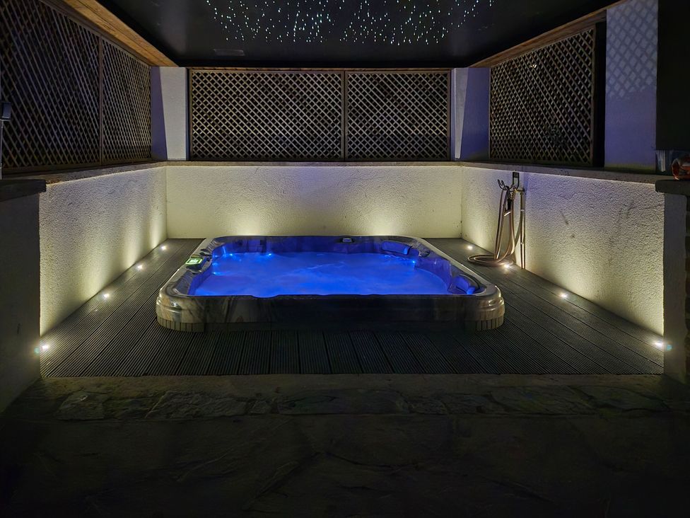 A hot tub surrounded by wooden deck and lighting at Mayflower Cottage in Lyme Regis