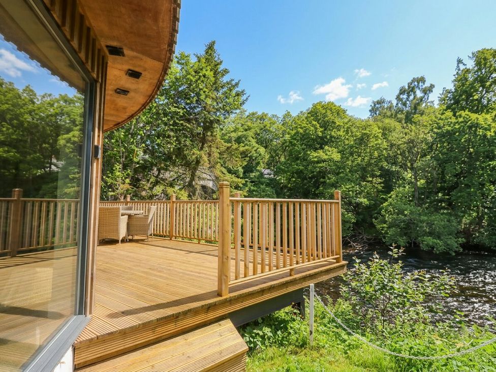 A wooden deck overlooking a river surrounded by trees at The Crannog in Killin