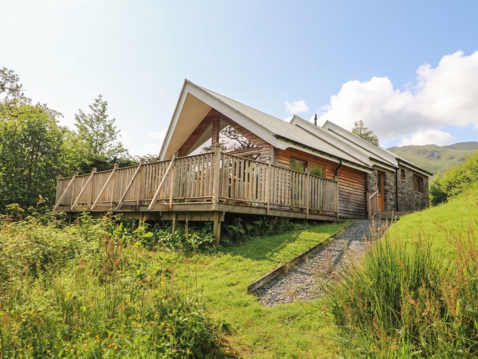 A house with a deck and steps in a grassy area at Riverbank Cottage Killin