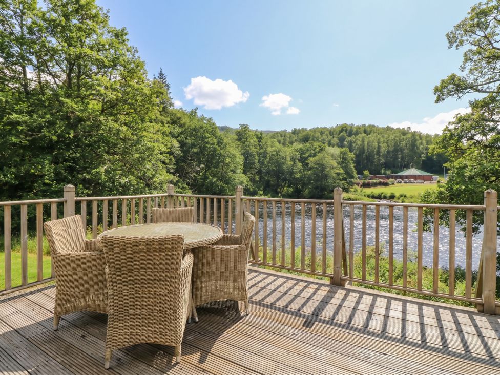 An outdoor area with a table and chairs overlooking a river at Riverbank Cottage in Killin