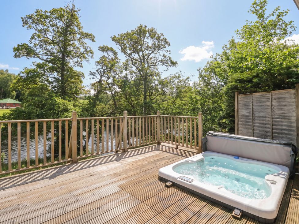 A deck with a hot tub overlooking trees and a river at Riverbank Cottage in Killin
