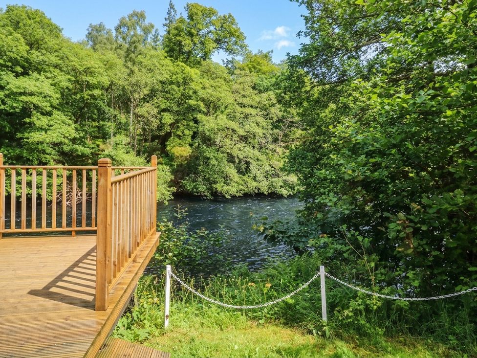 A deck overlooking a river surrounded by trees at Otter’s Holt in Killin