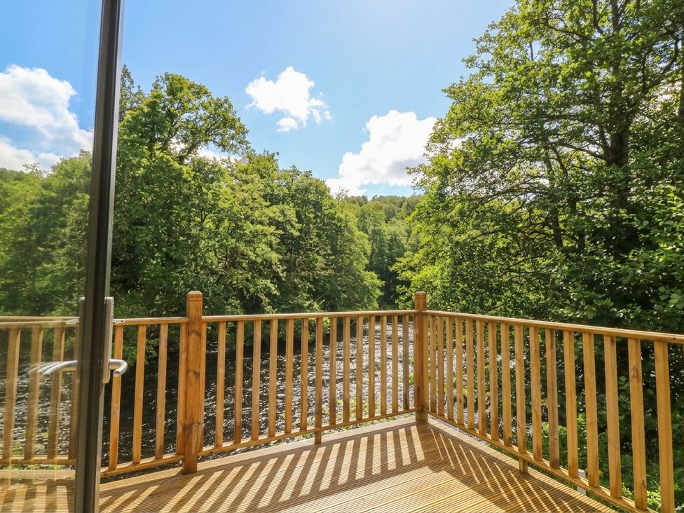 A deck overlooking a river surrounded by trees at Otter’s Holt in Killin