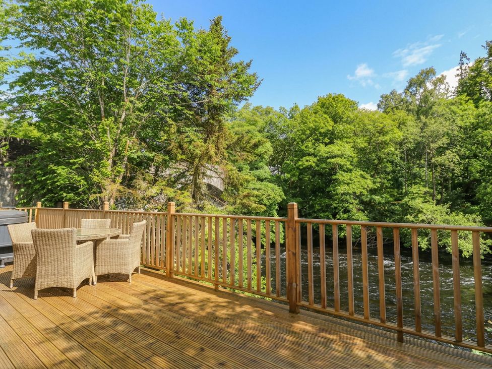 An outdoor deck with furniture overlooking a river at Otter’s Holt in Killin