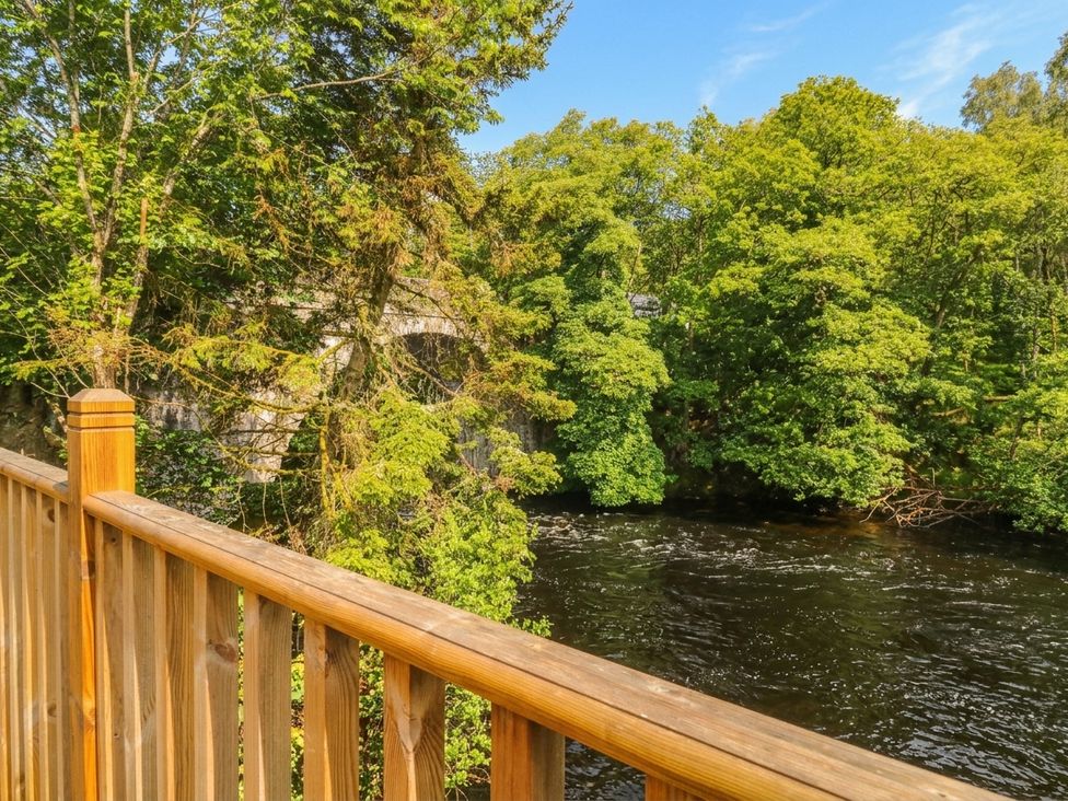 A river view with a wooden railing and trees at Otter’s Holt in Killin