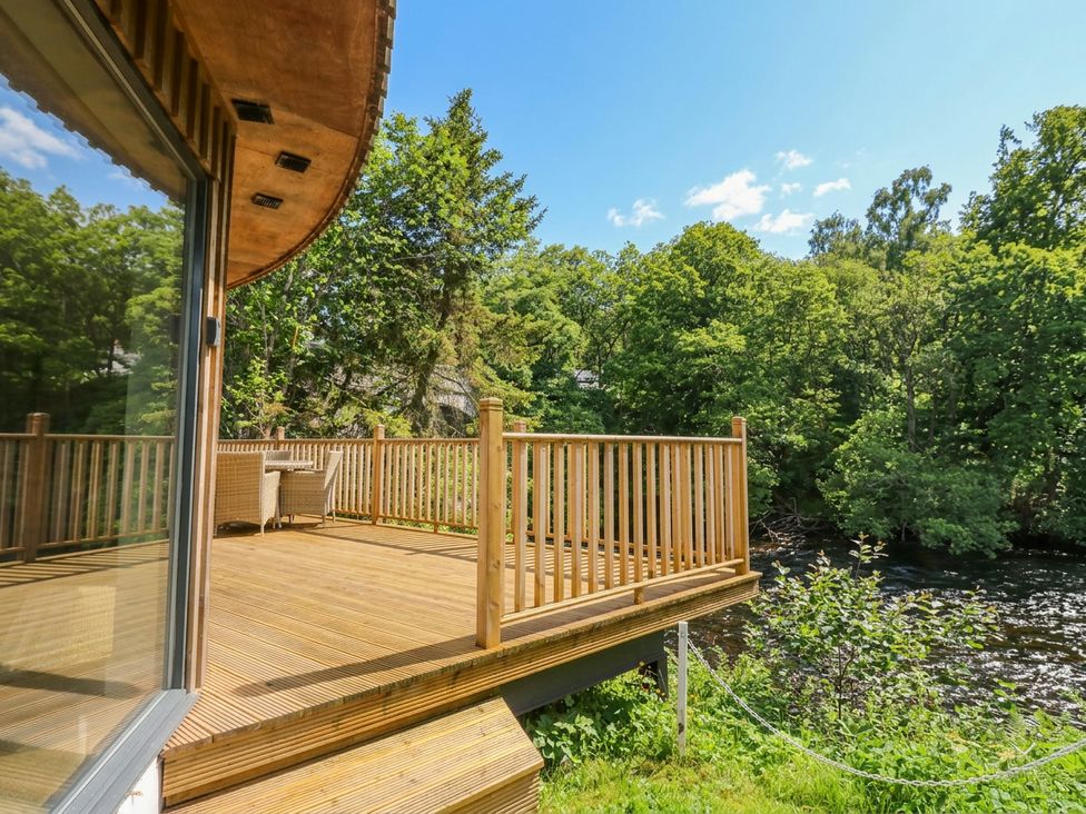 A deck overlooking a river with trees at Otter’s Holt in Killin