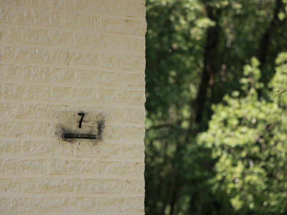 A house number 7 on a corner of a yellow brick wall in a wooded area at 7 Brunston Avenue