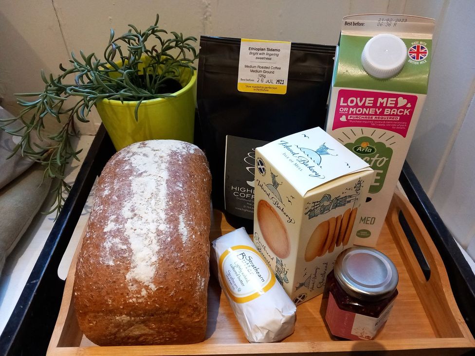 A kitchen scene with bread, coffee, milk, biscuits, jam, and a plant on a tray at Hollybirch in Crieff
