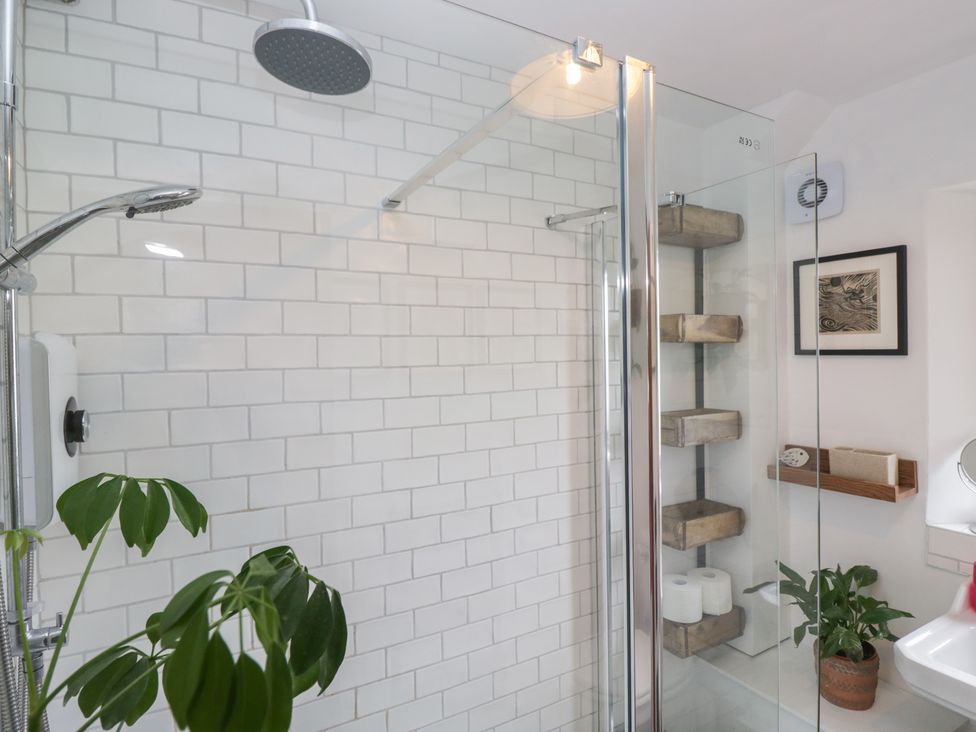 A shower with glass enclosure and shelving at Over Brow Cottage in Coniston