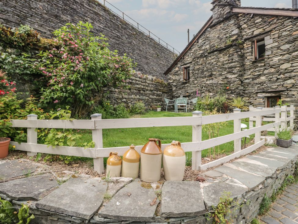 A garden with a stone wall and a fence at Over Brow Cottage in Coniston