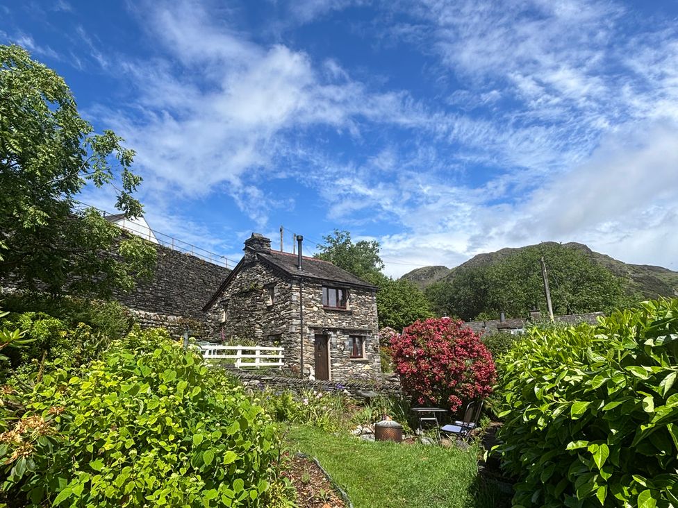 A stone cottage surrounded by flowers and mountains at Over Brow Cottage in Coniston