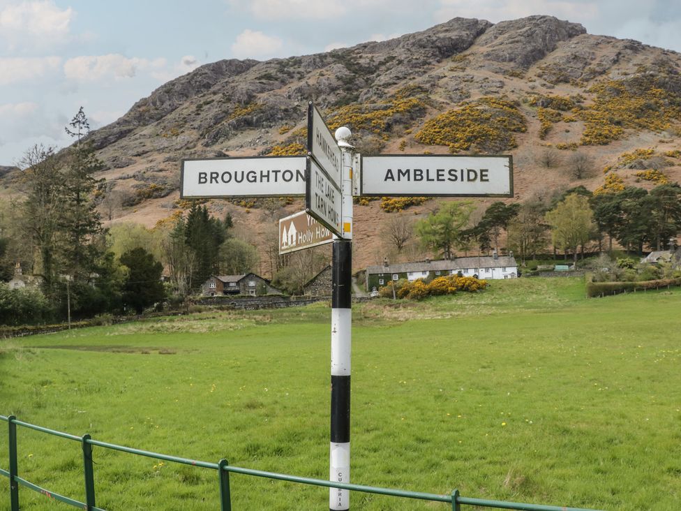 A signpost indicating directions to Broughton and Ambleside near a field and hillside in Coniston