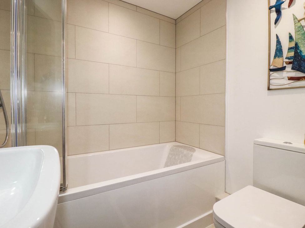 A bathroom with a bathtub, toilet, sink and decorative wall art at Little House in Wadebridge