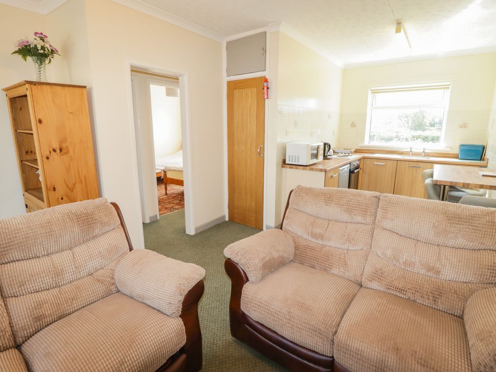 A living room with a sofa and kitchen area at Cottage 3 Tenby