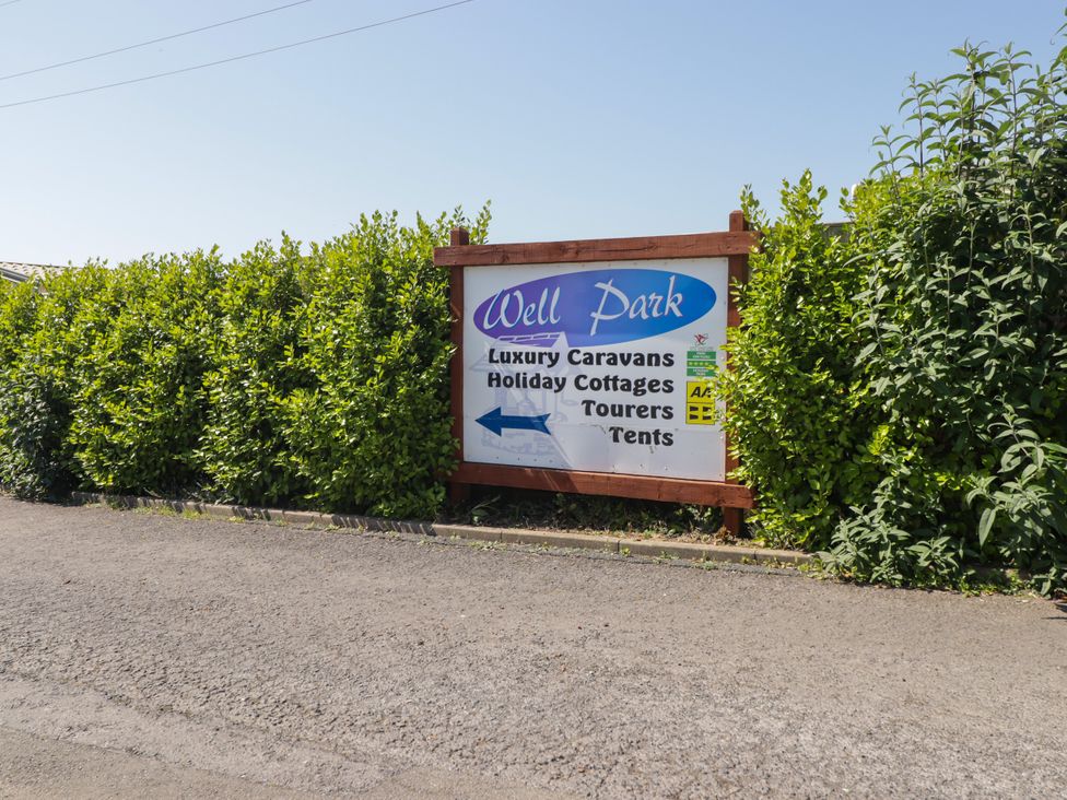 A sign displaying information about Well Park with hedges in Tenby