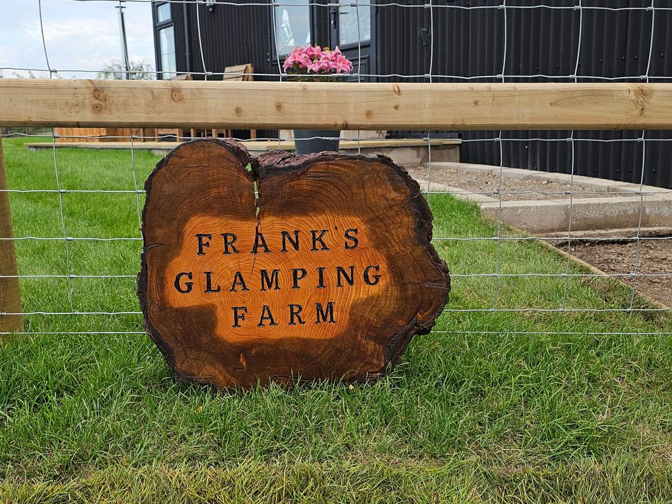 A wooden sign that says FRANK'S GLAMPING FARM with flowers at Frank's Glamping Farm in Nercwys near Mold