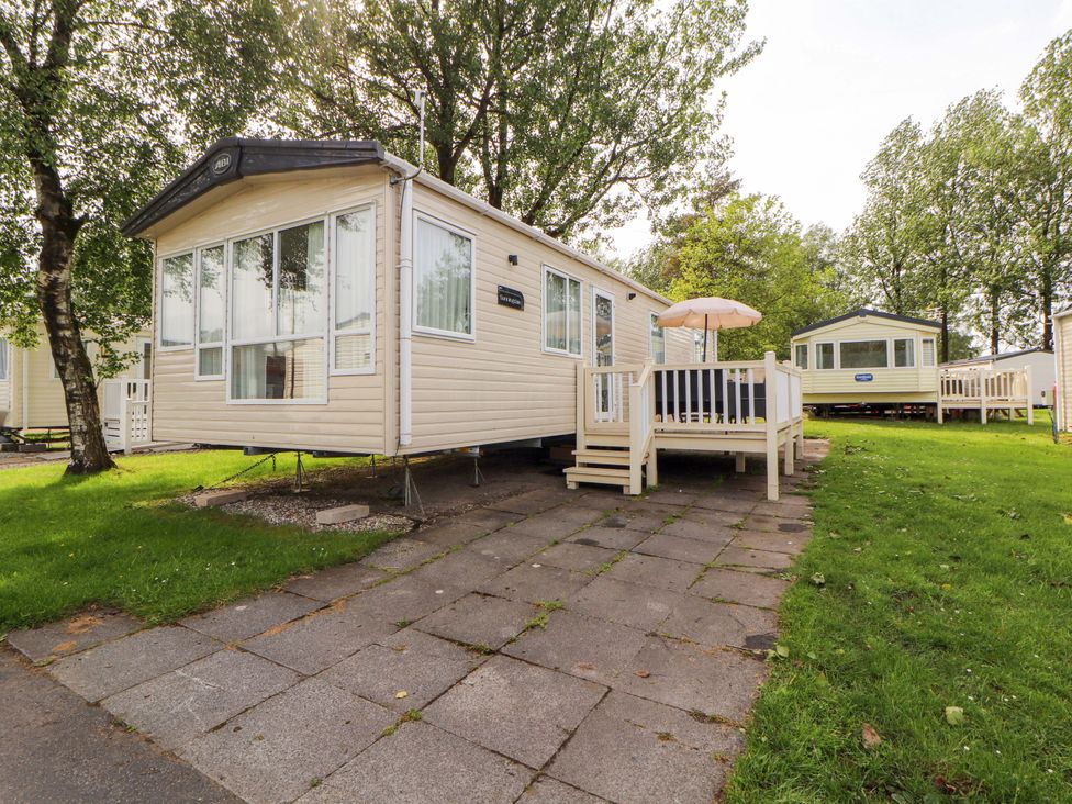 A caravan with decking and an umbrella in a green area at Caravan