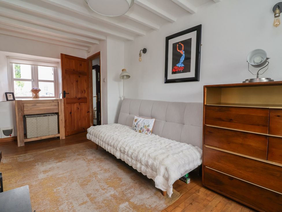 A living room with a sofa bed and a wooden drawer unit at Tenandeleven Cottage Denbigh