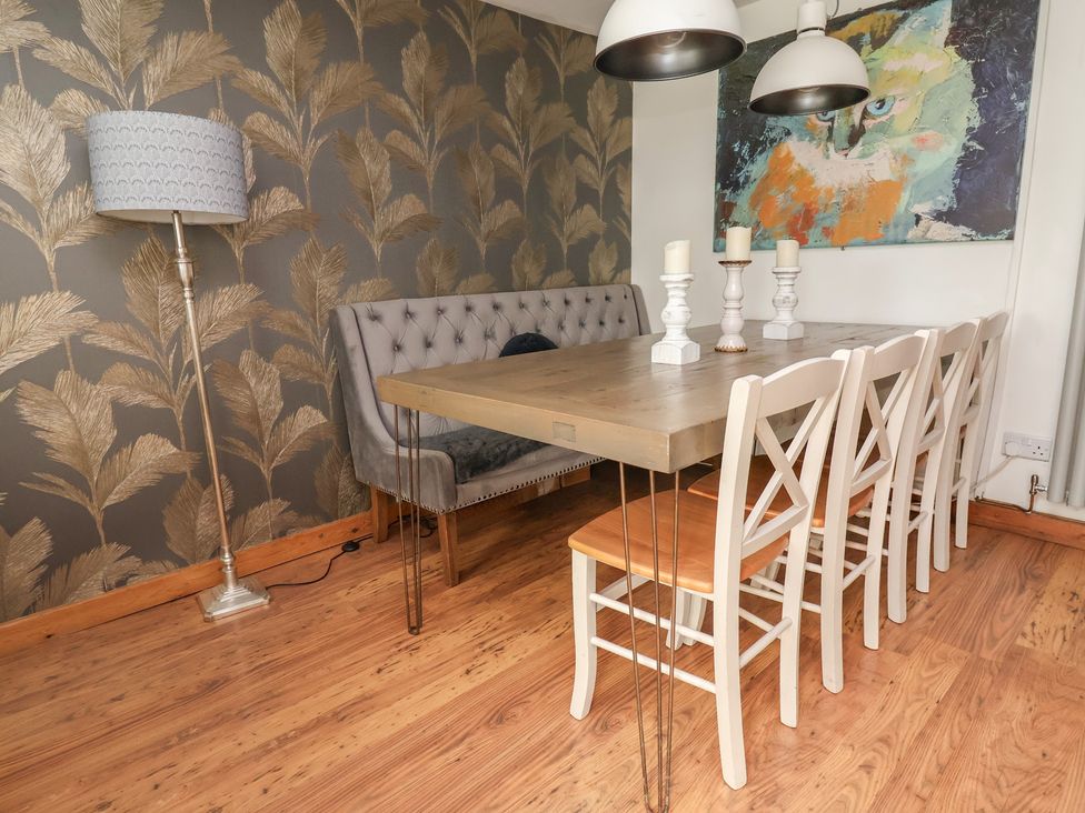 A dining room with a table, chairs, and artwork at Tenandeleven Cottage in Denbigh