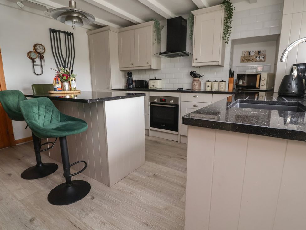 A kitchen with bar stools and appliances at Tenandeleven Cottage Denbigh