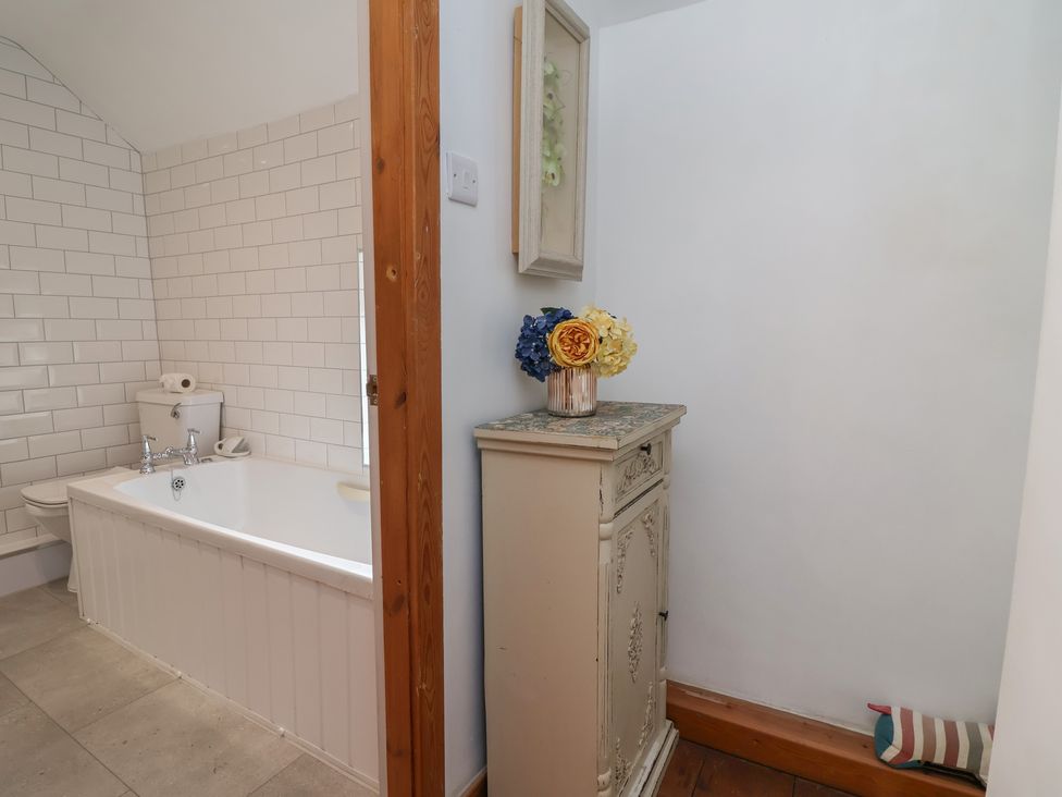 A bathroom featuring a bathtub, toilet, and cabinet at Tenandeleven Cottage in Denbigh
