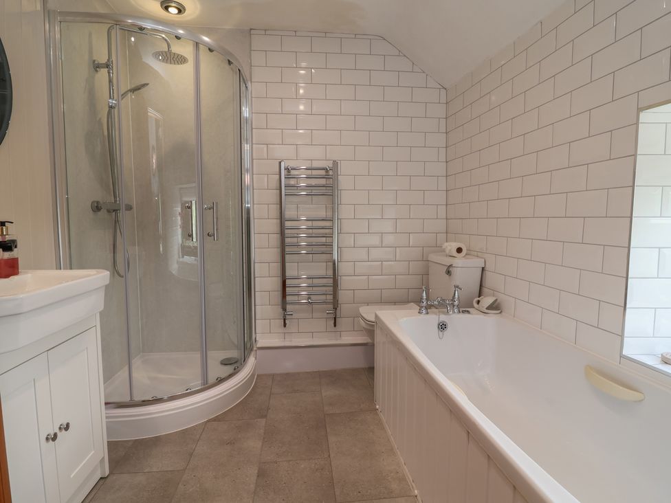 A bathroom with a shower, bathtub, toilet, and sink at Tenandeleven Cottage in Denbigh