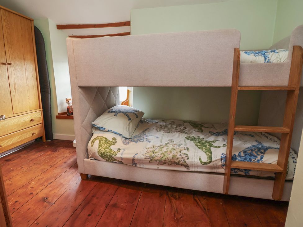 A bunk bed with a wooden wardrobe in the bedroom at Tenandeleven Cottage Denbigh