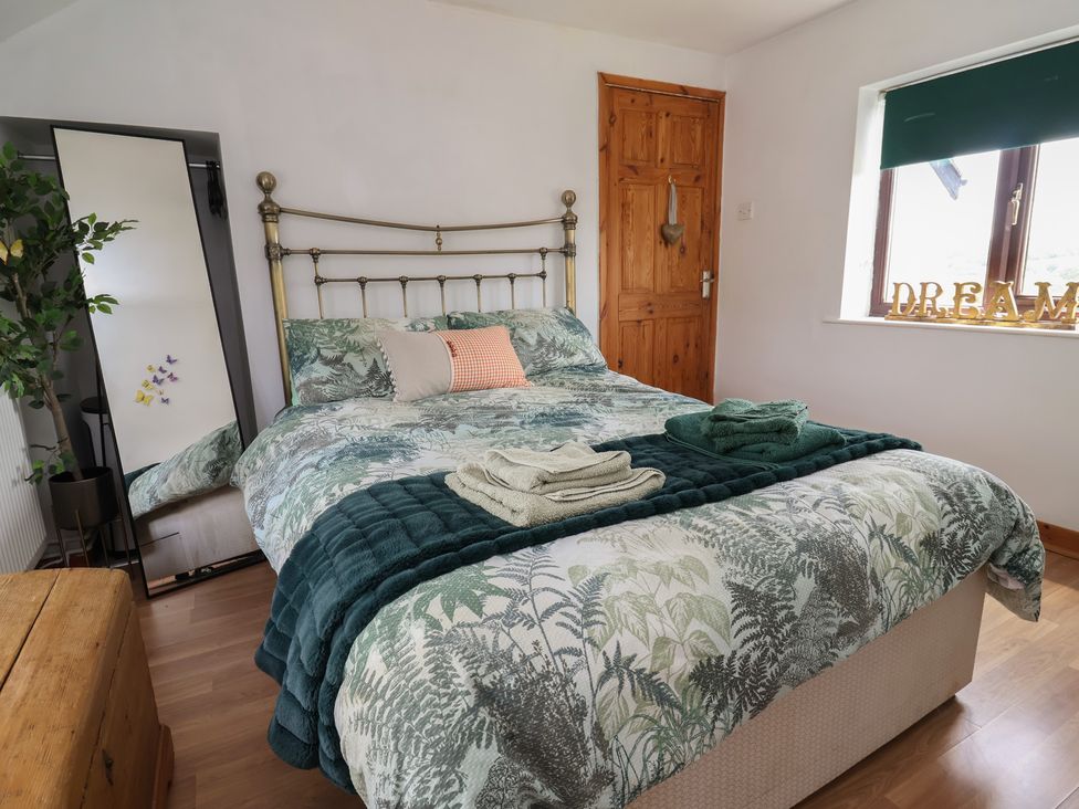 A bedroom with a bed and mirror at Tenandeleven Cottage in Denbigh
