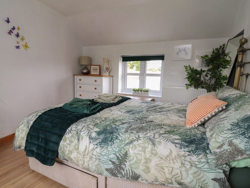 A bedroom with a bed covered in linens and a dresser with a lamp at Tenandeleven Cottage in Denbigh