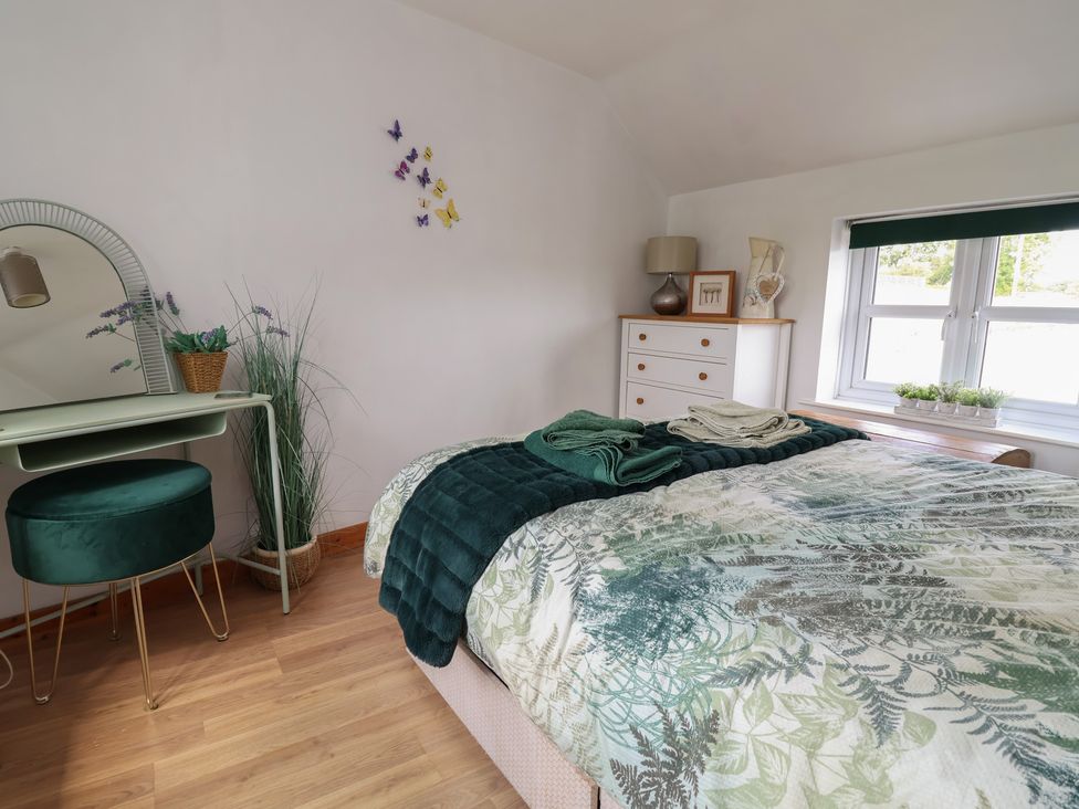 A bedroom with a bed and a mirror at Tenandeleven Cottage in Denbigh