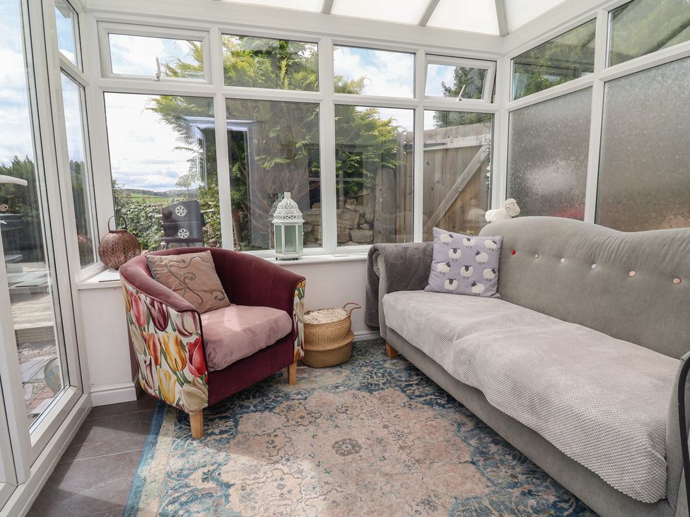A conservatory with a sofa and an armchair at Tenandeleven Cottage in Denbigh
