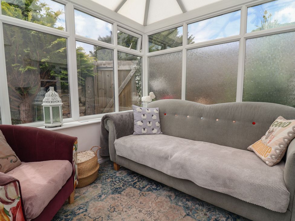 A conservatory with a sofa and armchair at Tenandeleven Cottage Denbigh