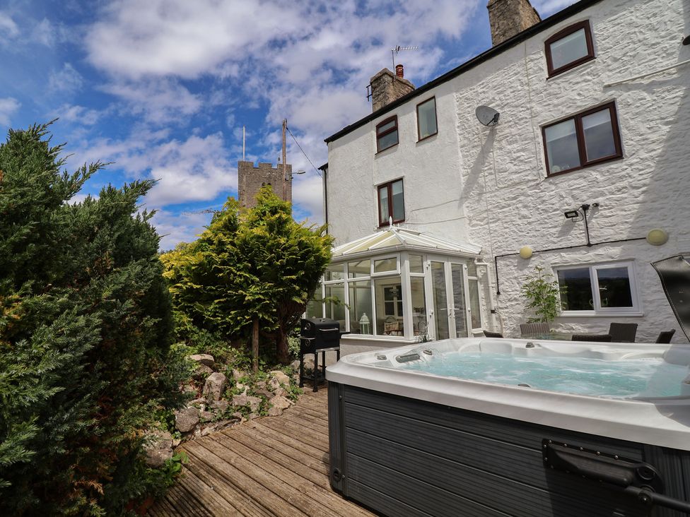 A garden with a hot tub and conservatory at Tenandeleven Cottage in Denbigh