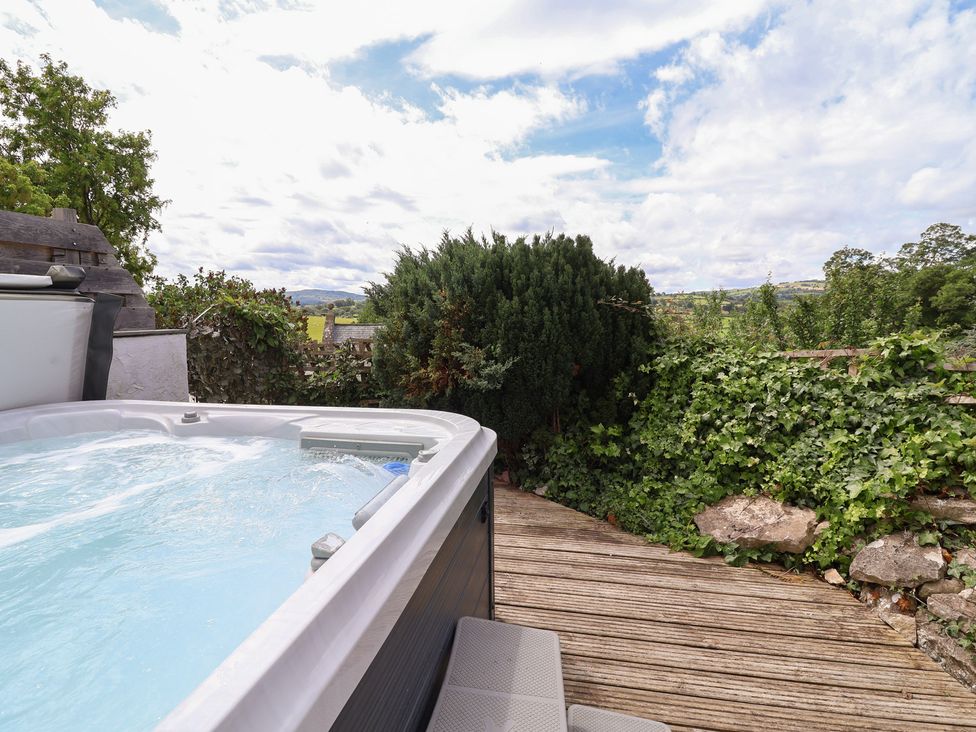 A hot tub on a deck surrounded by plants at Tenandeleven Cottage in Denbigh