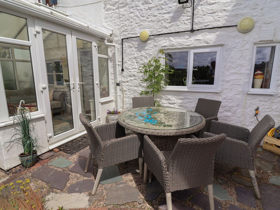 An outdoor dining area with a glass table and wicker chairs at Tenandeleven Cottage in Denbigh