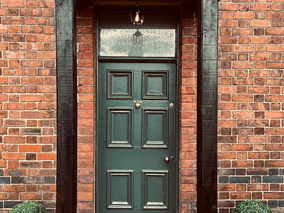 An entrance door with a brick wall and decorative hedge at Horseshoe Cottage in Macclesfield