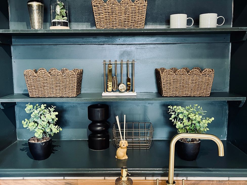 A shelf with plants, baskets, mugs, and utensils at Horseshoe Cottage in Macclesfield