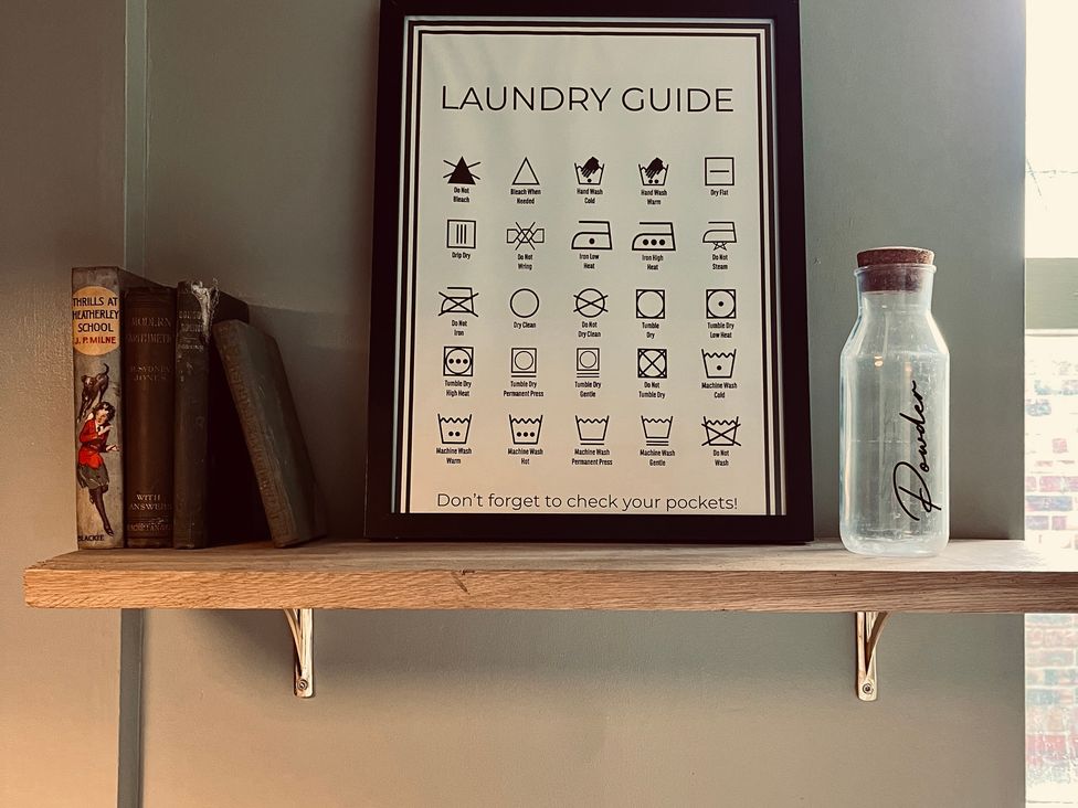 A laundry guide framed on a shelf with books and a bottle at Horseshoe Cottage in Macclesfield