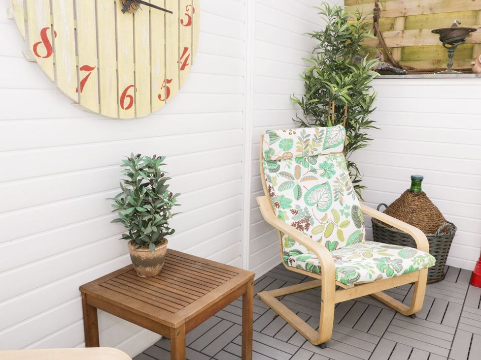 A snug area with a chair, table, clock, and plants at The Hideaways Tyn-y-Gongl