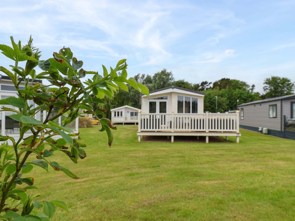 A cabin with a deck surrounded by grass and trees at Finch 66 Scarborough