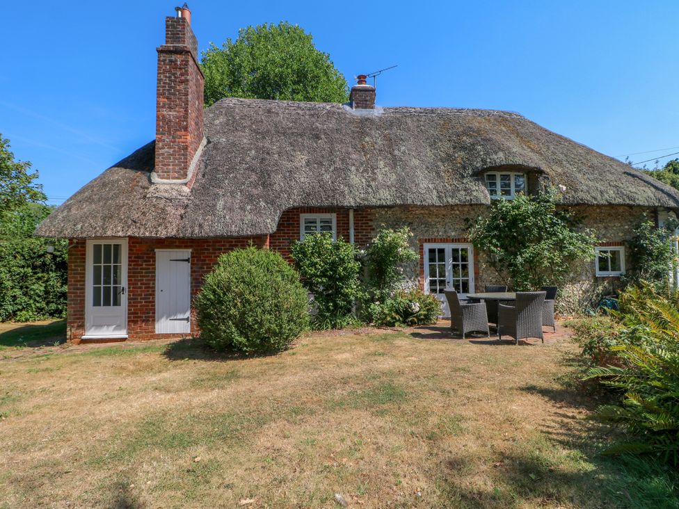 A cottage with a thatched roof and dining area in the garden at Little Owl High Cross near Petersfield