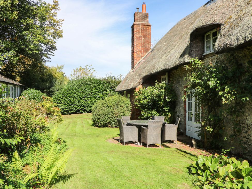A garden with a thatched cottage and patio furniture at Little Owl in High Cross near Petersfield