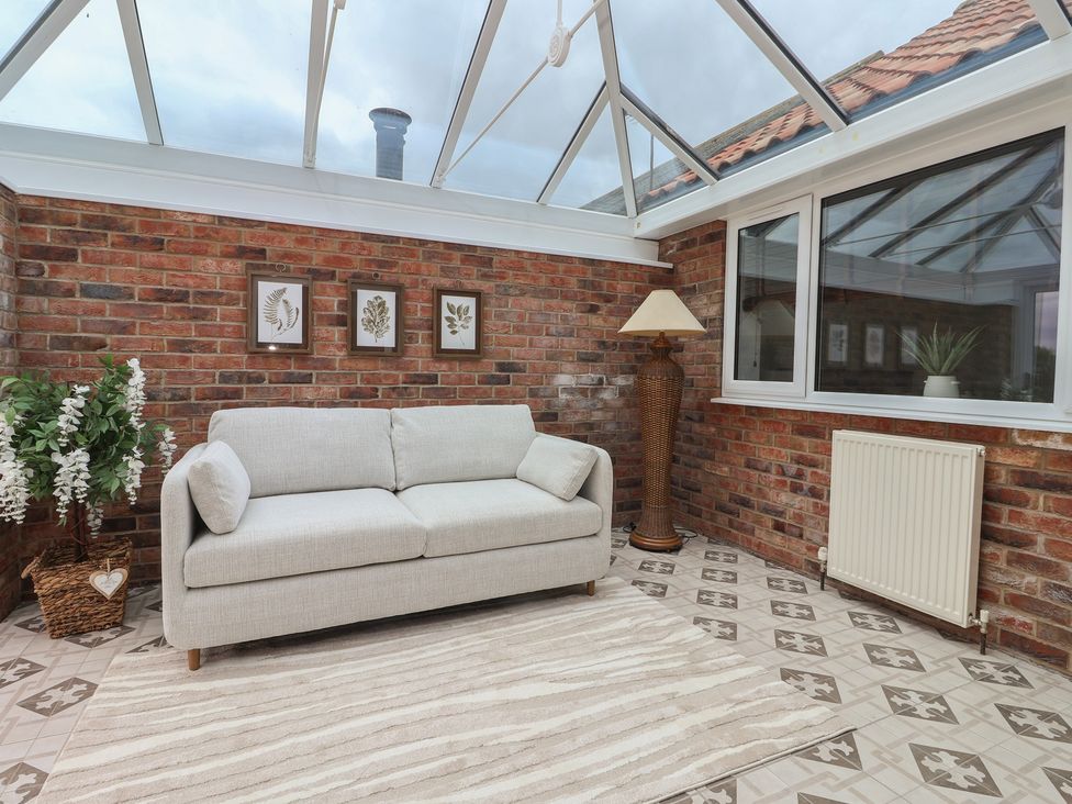 A conservatory with a sofa and plants at Gravel Pit Cottage in Bridlington