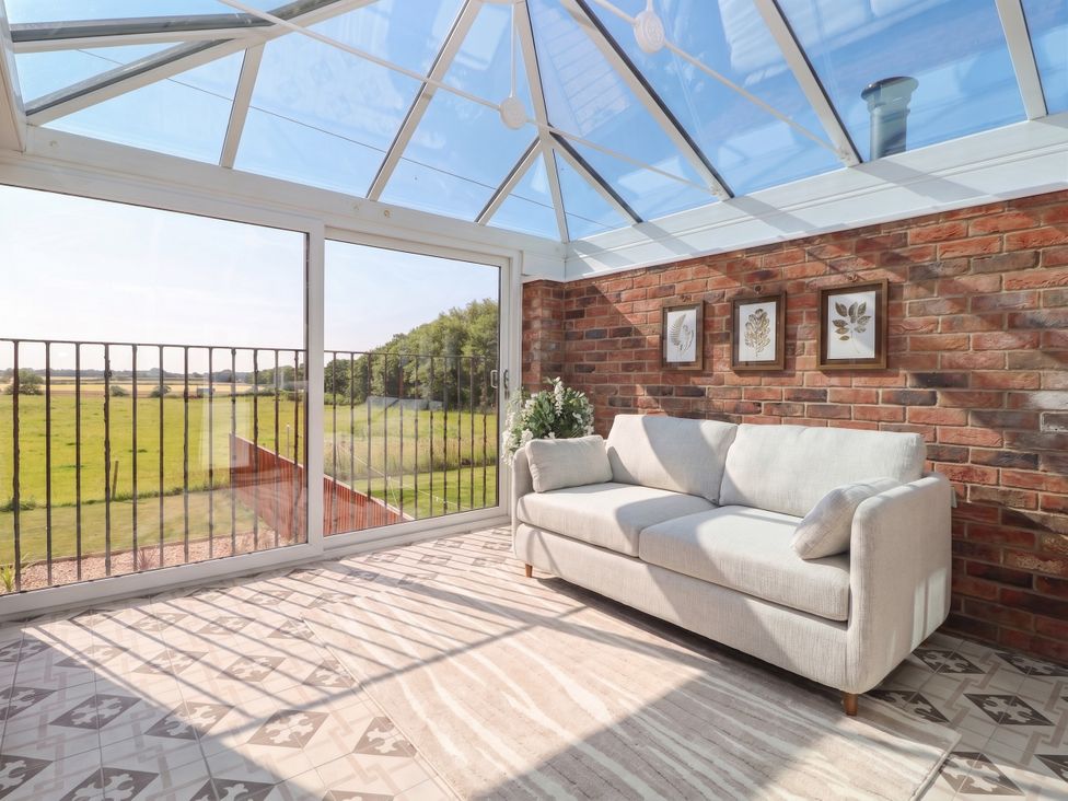 A conservatory with a sofa and a view of the garden at Gravel Pit Cottage in Bridlington