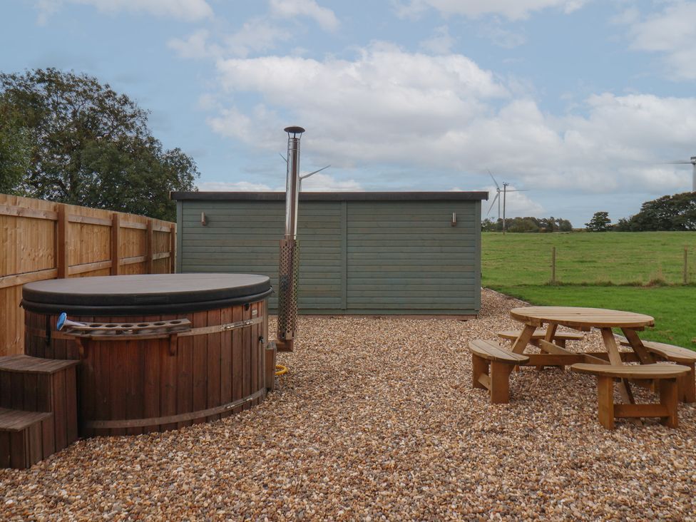 An outdoor area with a hot tub and wooden picnic table at Gravel Pit Cottage in Fraisthorpe