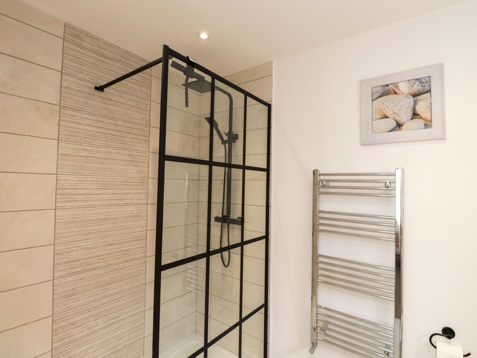 A bathroom with a glass shower and towel rail at 95 Cae America, Llanfairfechan