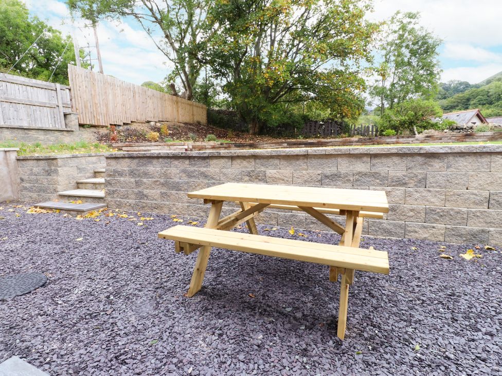 A garden with a wooden picnic table on gravel at 95 Cae America Llanfairfechan